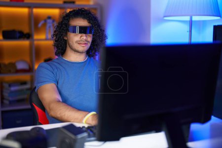 Téléchargez les photos : Jeune homme latin streamer jouer à un jeu vidéo en utilisant des lunettes de réalité virtuelle à la salle de jeux - en image libre de droit