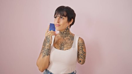 Foto de Mujer hispana con brazo amputado sosteniendo tarjeta de crédito pensando sobre fondo rosa aislado - Imagen libre de derechos
