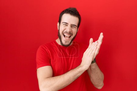 Téléchargez les photos : Jeune homme hispanique portant t-shirt rouge occasionnel applaudissements et applaudissements heureux et joyeux, souriant mains fiers ensemble - en image libre de droit