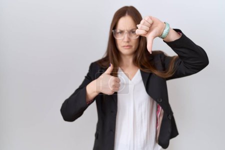 Photo for Beautiful brunette woman wearing business jacket and glasses doing thumbs up and down, disagreement and agreement expression. crazy conflict - Royalty Free Image
