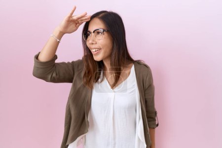 Téléchargez les photos : Femme chinoise du Moyen Âge portant des lunettes sur fond rose très heureux et souriant regardant loin avec la main sur la tête. concept de recherche. - en image libre de droit