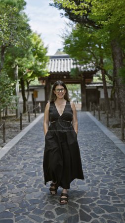 Photo for Cheerful, confident beautiful hispanic woman adorned with glasses standing tall, enjoying a walk, smiling radiantly for the camera at the zen ginkaku-ji temple garden in kyoto, japan. - Royalty Free Image