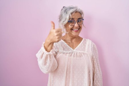 Photo for Middle age woman with grey hair standing over pink background doing happy thumbs up gesture with hand. approving expression looking at the camera showing success. - Royalty Free Image