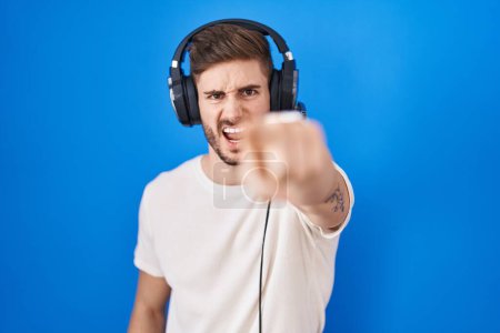 Photo for Hispanic man with beard listening to music wearing headphones pointing displeased and frustrated to the camera, angry and furious with you - Royalty Free Image