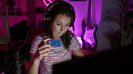 Téléchargez les photos : Une jeune femme examine une carte de crédit dans une salle de jeux éclairée au néon la nuit - en image libre de droit
