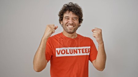 Téléchargez les photos : Jeune homme hispanique activiste portant l'uniforme bénévole faisant geste gagnant sur fond blanc isolé - en image libre de droit