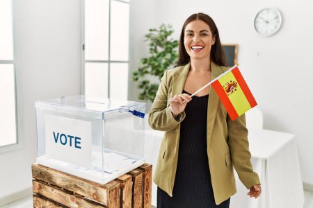 Photo for Young beautiful hispanic woman smiling confident holding spain flag standing at electoral college - Royalty Free Image