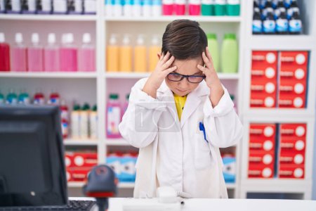 Photo for Young hispanic kid working at pharmacy drugstore with hand on head, headache because stress. suffering migraine. - Royalty Free Image