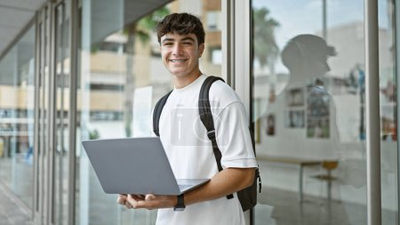 Photo for Cheerful hispanic teenager at university, a young, smart student enjoying laptop studies in the sunlight, backpack slung over a casual outfit. - Royalty Free Image