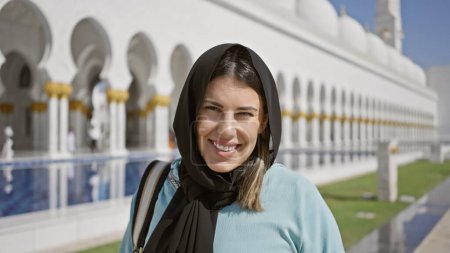 Photo for A smiling young adult woman wearing a hijab at a stunning uae mosque, embodying beauty and islamic tourism. - Royalty Free Image