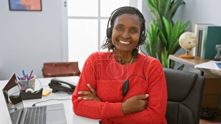 Téléchargez les photos : Femme afro-américaine souriant avec casque dans un environnement de bureau moderne - en image libre de droit