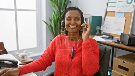 Téléchargez les photos : Femme africaine souriante avec écouteurs travaillant dans un bureau, représentant un représentant du service à la clientèle. - en image libre de droit