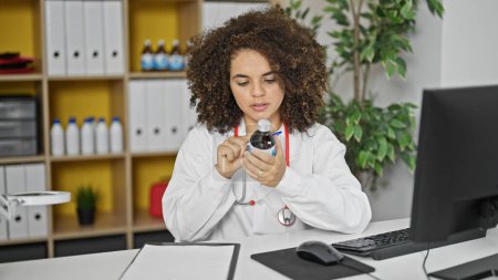 Photo for Young beautiful hispanic woman doctor using computer reading information of medication bottle at clinic - Royalty Free Image