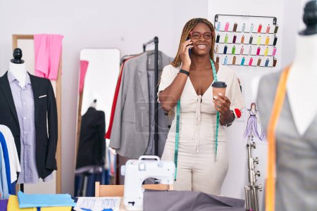 Téléchargez les photos : Femme afro-américaine tailleur parler sur smartphone boire du café au magasin de tailleur - en image libre de droit
