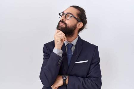 Téléchargez les photos : Hispanic man with beard wearing suit and tie with hand on chin thinking about question, pensive expression. smiling with thoughtful face. doubt concept. - en image libre de droit