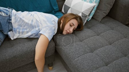 Foto de Una joven morena descansa tranquilamente en un sofá gris en un acogedor interior de la casa, encarnando la relajación y el confort doméstico. - Imagen libre de derechos