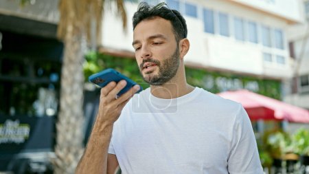 Téléchargez les photos : Jeune homme hispanique envoyant un message vocal avec smartphone dans la rue - en image libre de droit