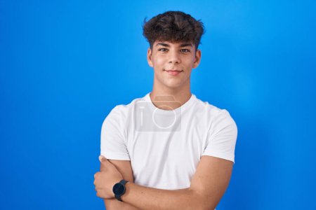 Photo for Hispanic teenager standing over blue background happy face smiling with crossed arms looking at the camera. positive person. - Royalty Free Image