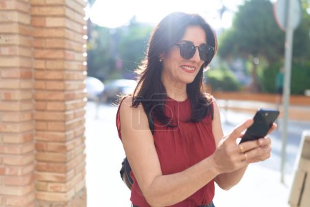 Téléchargez les photos : Moyen Age femme hispanique souriant confiant en utilisant smartphone à la rue - en image libre de droit