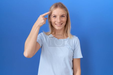 Téléchargez les photos : Jeune femme caucasienne portant un t-shirt bleu décontracté souriant pointant vers la tête avec un doigt, grande idée ou pensée, bonne mémoire - en image libre de droit