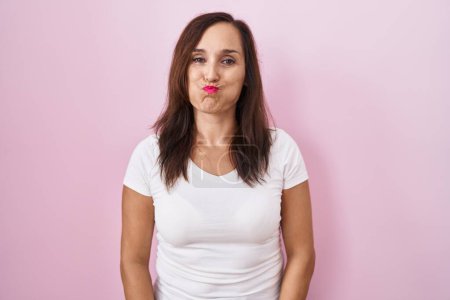 Photo for Middle age brunette woman standing over pink background puffing cheeks with funny face. mouth inflated with air, crazy expression. - Royalty Free Image