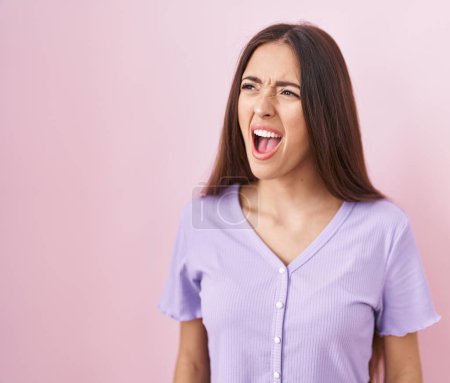 Téléchargez les photos : Young hispanic woman with long hair standing over pink background angry and mad screaming frustrated and furious, shouting with anger. rage and aggressive concept. - en image libre de droit