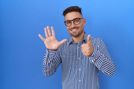 Foto de Hombre hispano con barba con gafas mostrando y señalando con los dedos número seis mientras sonríe confiado y feliz. - Imagen libre de derechos