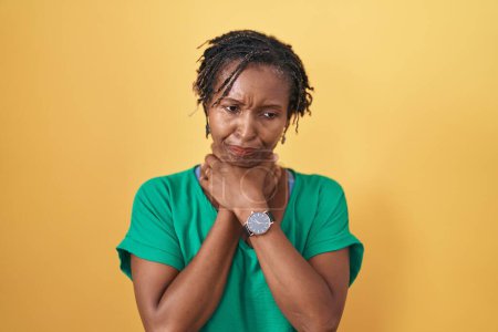Foto de Mujer africana con rastas de pie sobre fondo amarillo gritando sofocado porque estrangulamiento doloroso. problema de salud. concepto de asfixia y suicidio. - Imagen libre de derechos