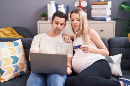 Photo for Man and woman couple using laptop and credit card expecting baby at home - Royalty Free Image