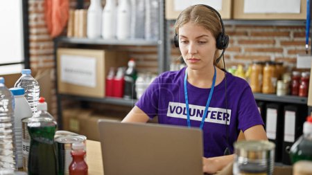 Téléchargez les photos : Jeune femme blonde bénévole ayant appel vidéo assis sur la table au centre de bienfaisance - en image libre de droit