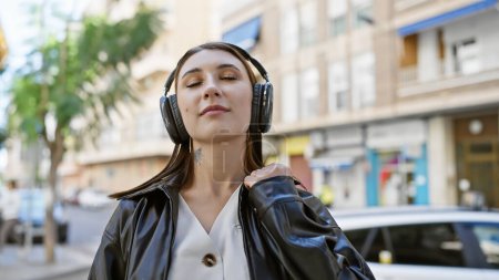 Téléchargez les photos : Une jeune femme brune aime la musique avec des écouteurs dans une rue de la ville, dépeignant la vie urbaine décontractée. - en image libre de droit