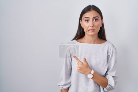 Photo for Young hispanic woman standing over white background pointing aside worried and nervous with forefinger, concerned and surprised expression - Royalty Free Image