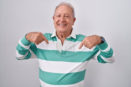 Téléchargez les photos : Homme âgé avec les cheveux gris debout sur fond blanc regardant confiant avec le sourire sur le visage, se montrant du doigt fier et heureux. - en image libre de droit