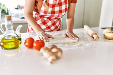 Photo for Young beautiful hispanic woman kneading dough pizza with hands at the kitchen - Royalty Free Image