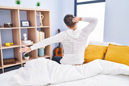 Foto de Joven hombre hispano despertando estirando los brazos en la vista trasera en el dormitorio - Imagen libre de derechos