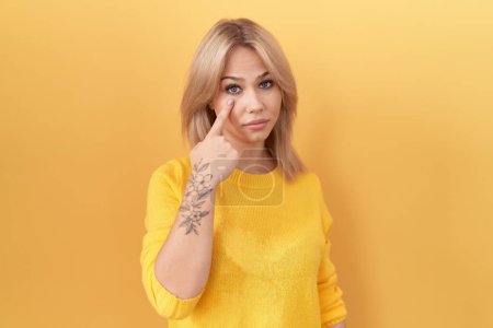 Téléchargez les photos : Jeune femme caucasienne portant un pull jaune pointant vers l'œil vous regardant geste, expression suspecte - en image libre de droit