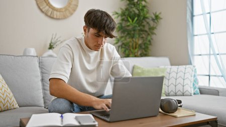 Concentrated young hispanic male student, engrossed in online education, sitting on cozy living room sofa, focused on laptop screen, relaxing at home, surrounded by technology