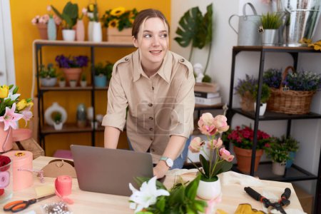 Téléchargez les photos : Young caucasian woman florist smiling confident using laptop at flower shop - en image libre de droit