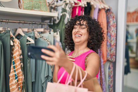 Téléchargez les photos : Jeune femme du Moyen-Orient client souriant confiant ayant appel vidéo au magasin de vêtements - en image libre de droit
