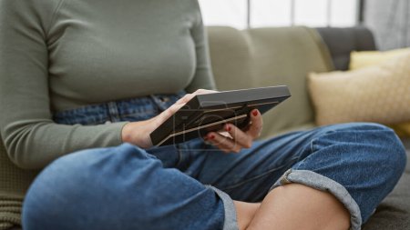 Foto de Una mujer lee un libro sobre un sofá en su moderna sala de estar, retratando la relajación, el ocio y la comodidad. - Imagen libre de derechos