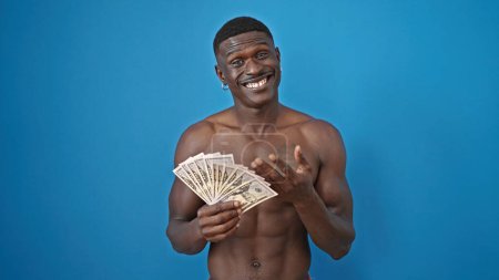 Téléchargez les photos : Africain américain debout torse nu comptant des dollars sur fond bleu isolé - en image libre de droit