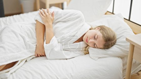 Téléchargez les photos : Jeune femme blonde souffrant de douleurs menstruelles couchée sur le lit dans la chambre - en image libre de droit