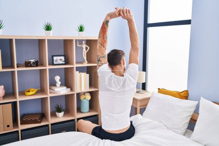 Photo for Young man waking up stretching arms on back view at bedroom - Royalty Free Image