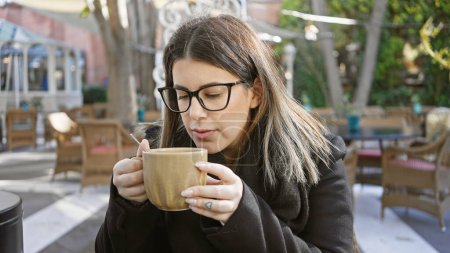 Téléchargez les photos : Jeune femme hispanique adulte dégustant un café à l'extérieur sur une terrasse d'un café - en image libre de droit