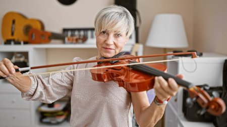 Photo for A mature woman with grey hair plays the violin in a music studio, showcasing talent and passion. - Royalty Free Image