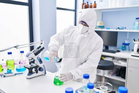 Photo for Young hispanic man scientist wearing medical mask pouring liquid on test tube at laboratory - Royalty Free Image