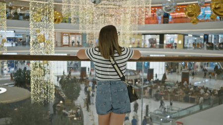 Téléchargez les photos : Vue arrière d'une femme brune admirant l'intérieur d'un luxueux centre commercial dubai avec des décorations suspendues. - en image libre de droit