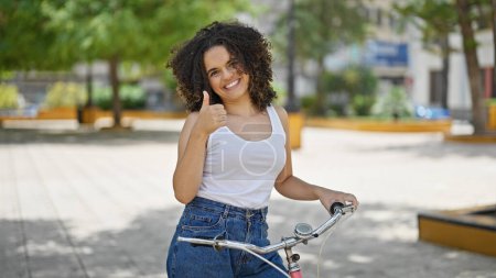 Téléchargez les photos : Jeune belle hispanique femme à vélo faisant pouce vers le haut geste au parc - en image libre de droit