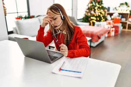 Foto de Joven caucásico mujer call center agente estresado teletrabajo sentado por árbol de Navidad en casa - Imagen libre de derechos