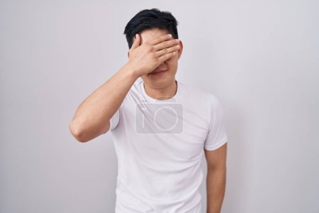 Photo for Young asian man standing over white background smiling and laughing with hand on face covering eyes for surprise. blind concept. - Royalty Free Image
